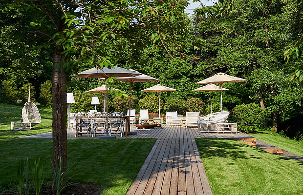Terrasse mit mehreren Sitzmöglichkeiten und Sonnenschirm mitten auf einer grünen Wiese