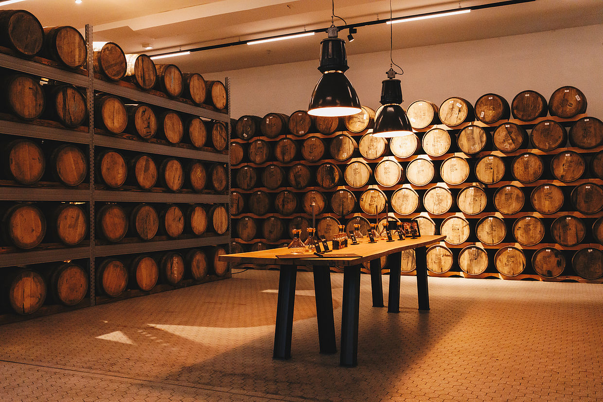 Holztisch für eine Weinverkostung, umgeben von Regalen mit Weinfässern darauf