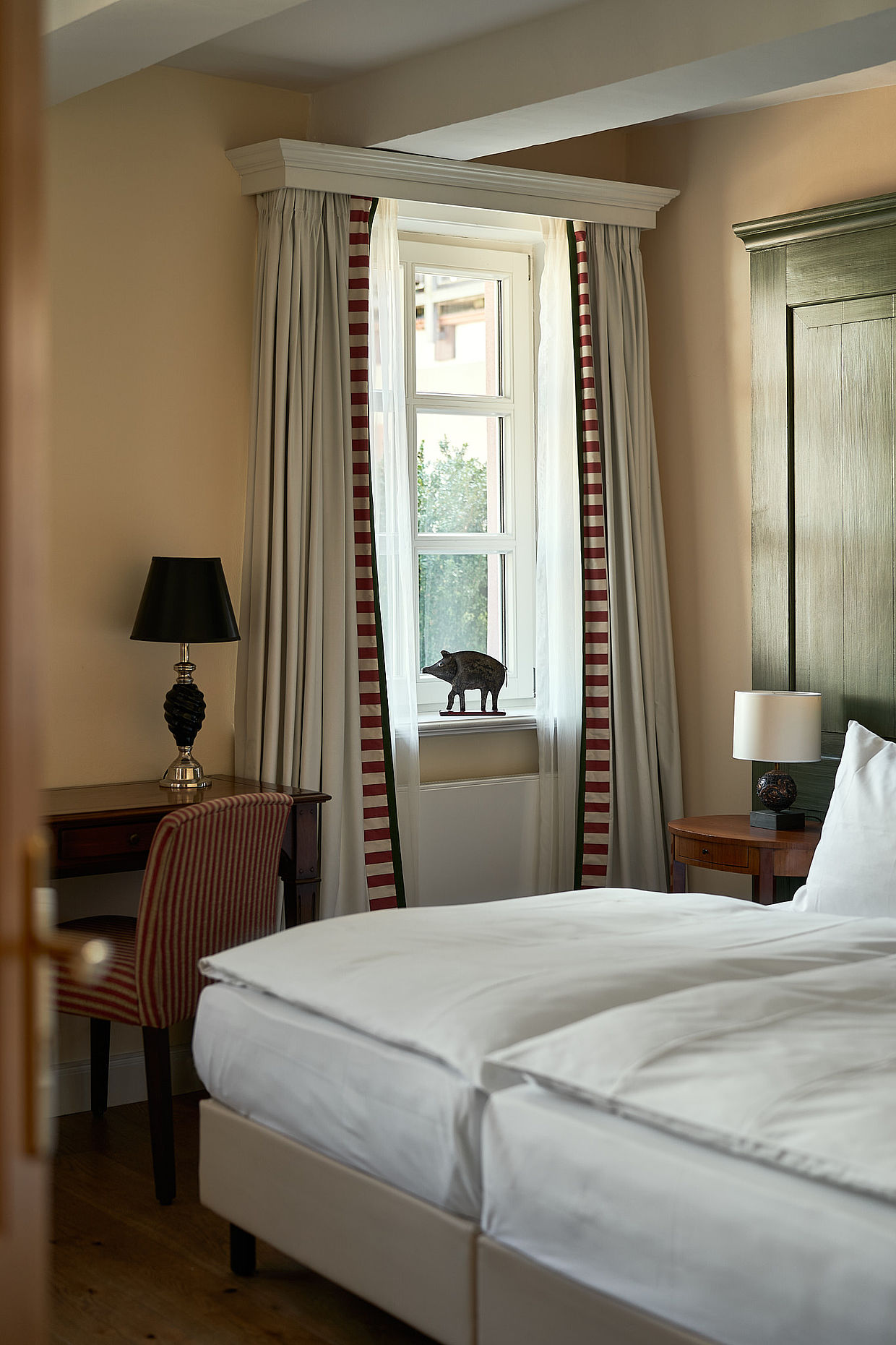 Doppelbett neben einem Fenster mit Vorhängen und einem dekorativen Wildschwein auf der Fensterscheibe