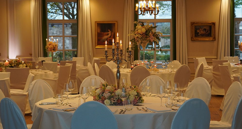 Festlich gedeckter Bankettsaal mit runden Tischen, Blumenschmuck und Kerzenleuchtern für eine elegante Hochzeitsfeier.
