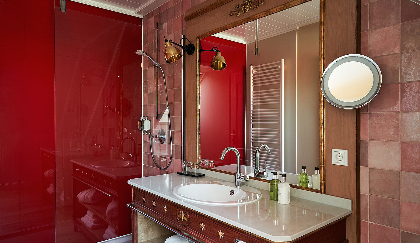 Ein Waschbecken und eine Duschkabine mit roter Wand im Badezimmer des Deluxe Mühle Zimmers