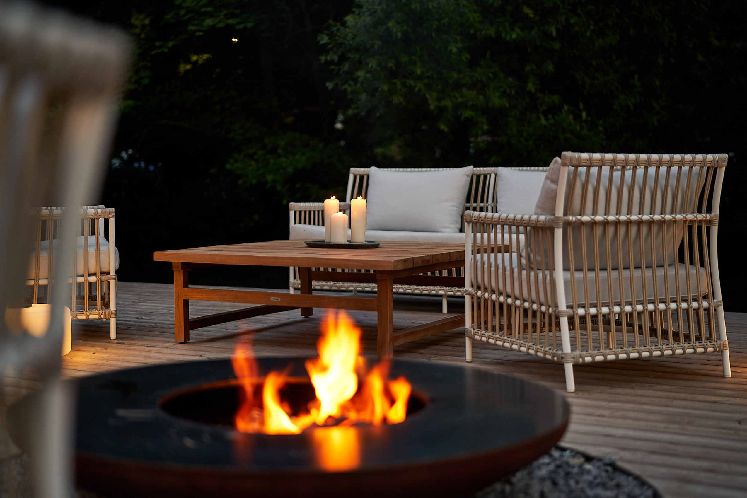 Gemütliche Outdoor-Lounge mit Feuerstelle, Rattansesseln, Tisch und Kerzen