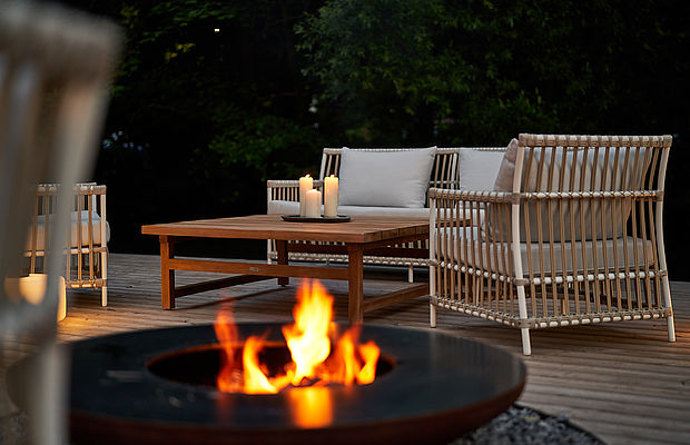 Gemütliche Outdoor-Lounge mit Feuerstelle, Rattansesseln, Tisch und Kerzen