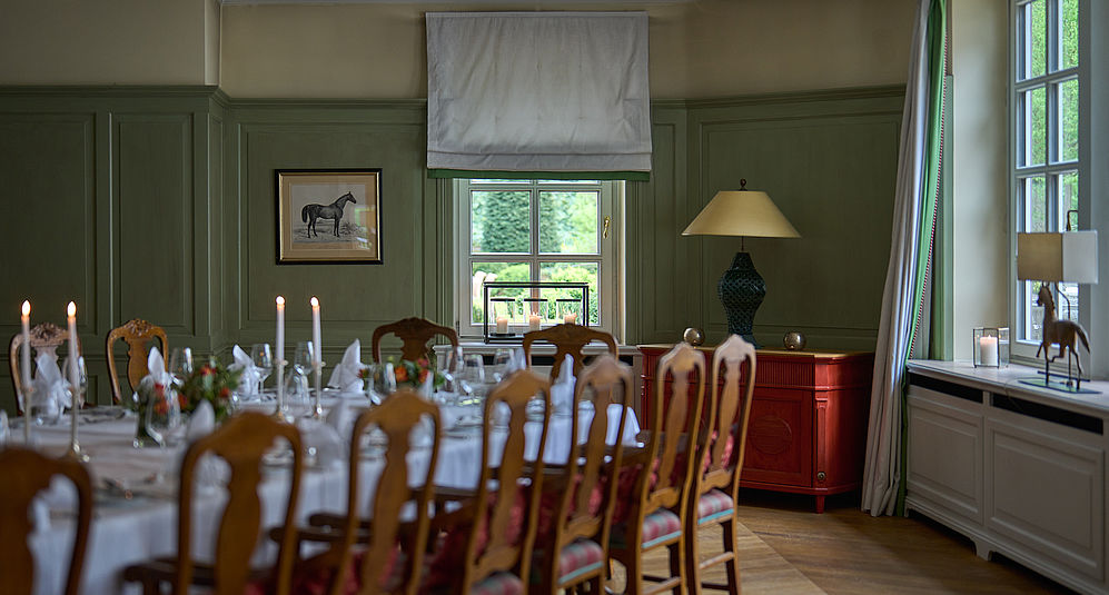Langer Tisch für ein Abendessen für mehrere Personen neben zwei Fenstern mit Blick auf einen Garten