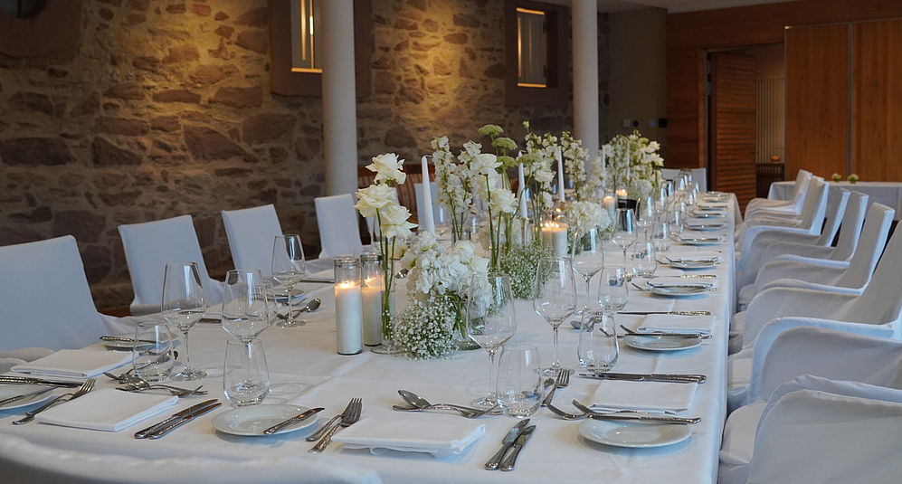 Eleganter Festsaal im Hardenberg Burghotel mit langer Tafel, weißen Stuhlhussen, Blumenschmuck und Kerzen für eine Hochzeit.
