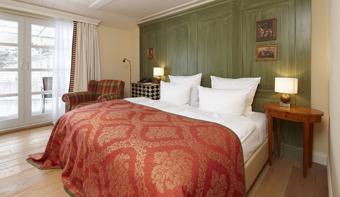 Doppelbett mit rotem Bettbezug unter einer grünen Wand, ein hölzerner Nachttisch und ein bunter Stuhl im Zimmer Cozy mit Balkon
