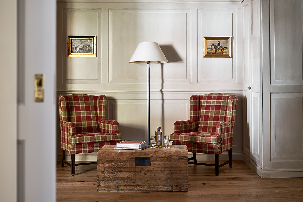Blick auf zwei karierte Stühle, eine Lampe und ein Tisch in Form einer Holzkiste