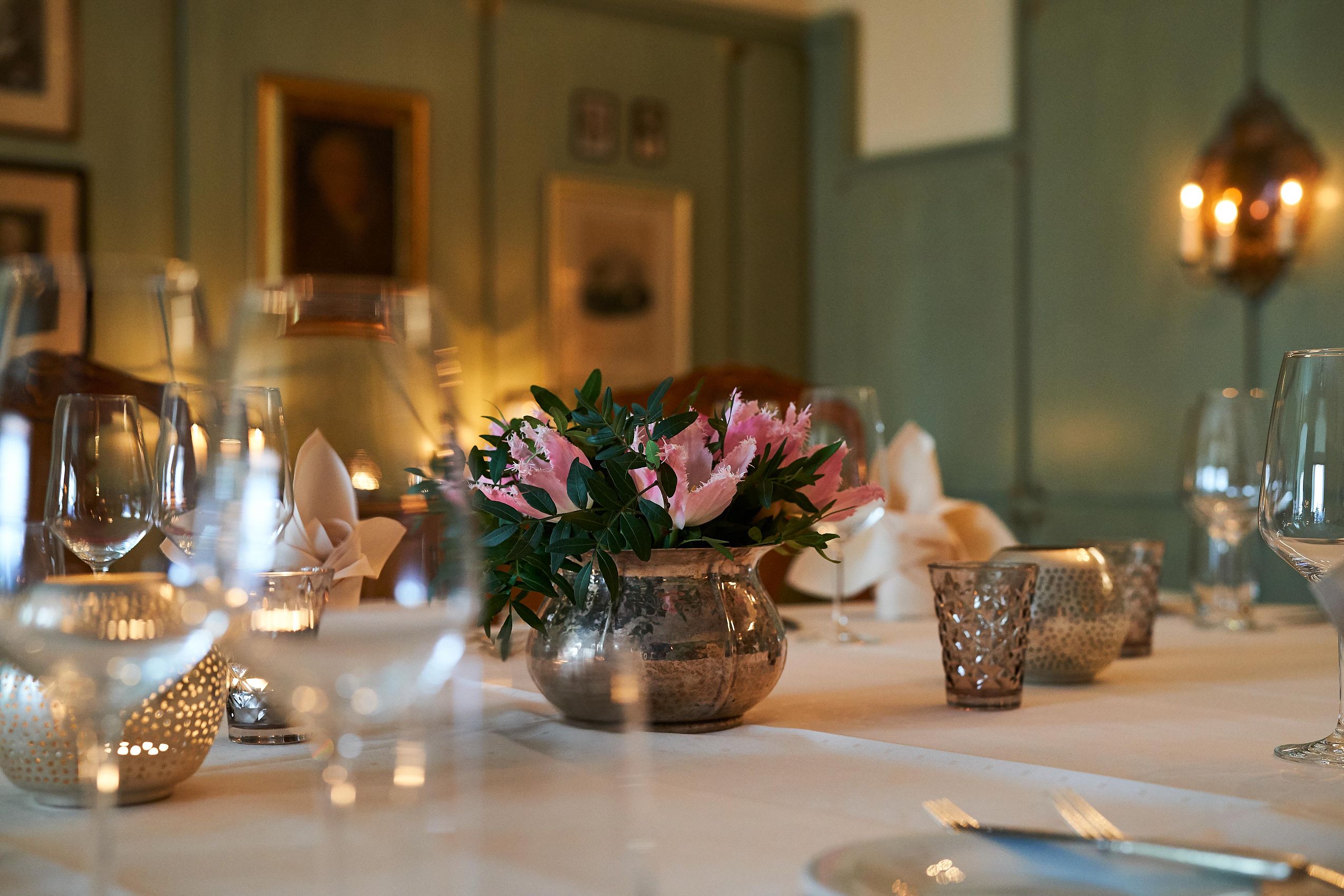 Großansicht von dekorativen rosa Blumen in einer goldenen Vase und von verschiedenen Gläsern auf einem Tisch