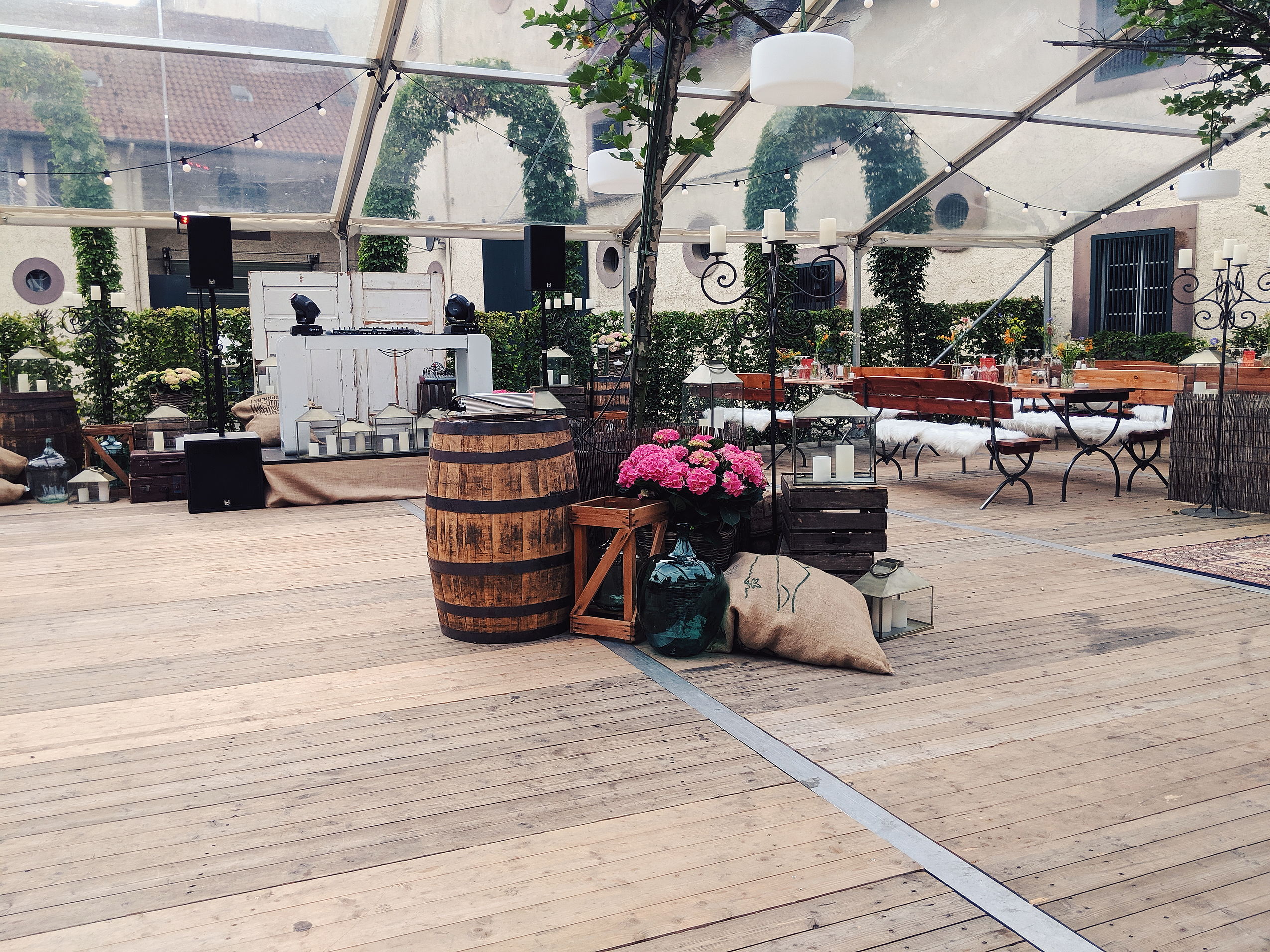 Outdoor-Hochzeitslocation mit Blumen, Holzbänken und Deko-Fässern.